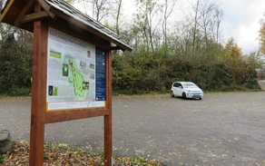 Parkplatz mit einem weißen geparkten Auto, im Vordergrund eine Informationstafel.