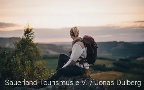 Frau sitzt auf einem Felsen und schaut in die Ferne.