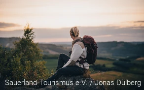 Frau sitzt auf einem Felsen und schaut in die Ferne.