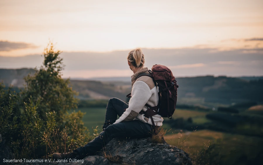 Frau sitzt auf einem Felsen und schaut in die Ferne.