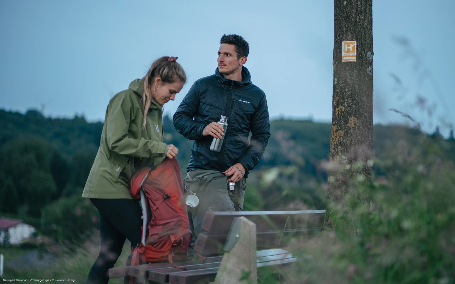 Zwei Wanderer  stehen an einer Bank am Sauerland-Höhenflug und packen ihren Rucksack