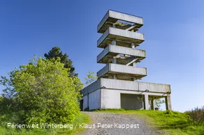 Turm aus Beton mit mehreren Etagen und Treppenaufgängen vor blauem Himmel.