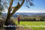 Ein Mann sitzt im Baum und genießt die Aussicht auf den Biggesee. Eine Frau macht im Hintergund ein Selfie am Sauerland-Höhenflug