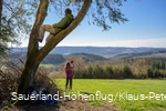 Ein Mann sitzt im Baum und genießt die Aussicht auf den Biggesee. Eine Frau macht im Hintergund ein Selfie am Sauerland-Höhenflug