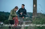 Zwei Wanderer  stehen an einer Bank am Sauerland-Höhenflug und packen ihren Rucksack
