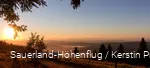 Blick in die Ferne, blauer Himmel, links die aufgehende Sonne, Heidelandschaft und ein paar Nadelbäume. Im Hintergrund sieht man sauerländer Berge.