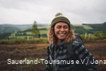 Eine Frau steht in Wanderausrüstung in einer idyllischen Landschaft und ist sichtlich glücklich